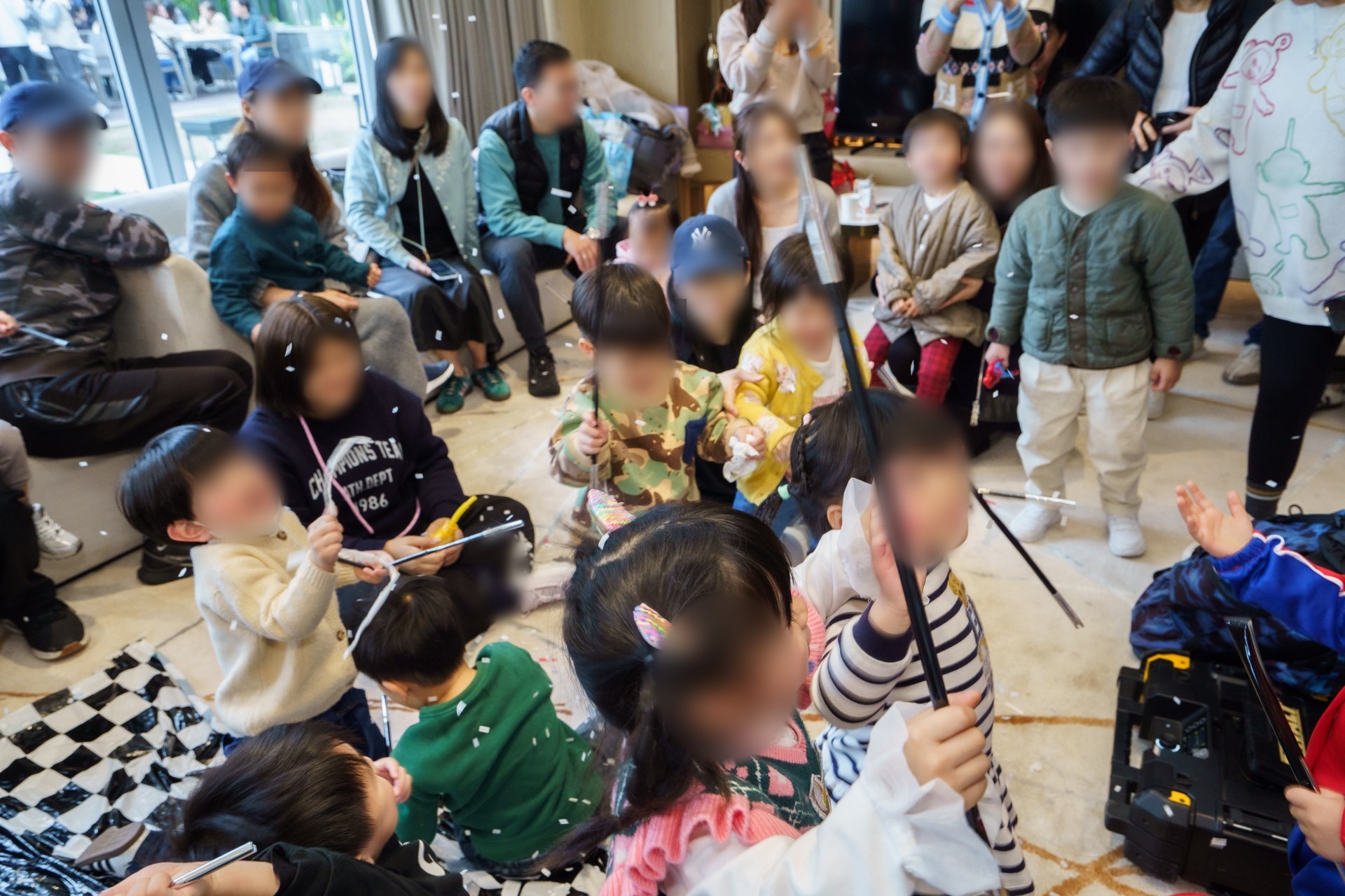 一場賽車主題的兒童生日會，小朋友坐在黑白格地墊上揮動魔術棒，彩紙在空中飄落，家長坐在後方梳化